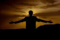 A solitary silhouette of a man stretching his arms against a vivid golden sunset, exuding calm and strength.